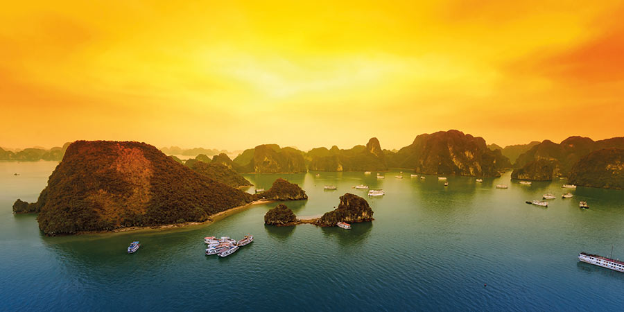 Ha Long Bay features deep blue waters, green mountainous islands and a rich yellow sky. 